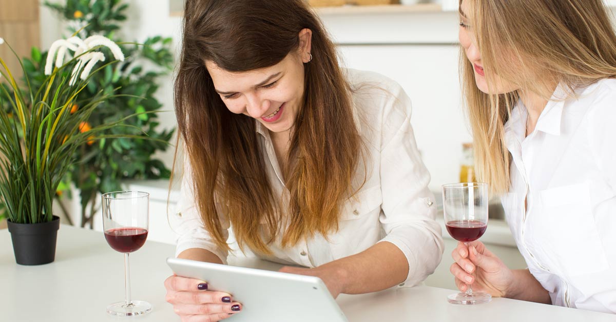 Women drinking wine while shopping online